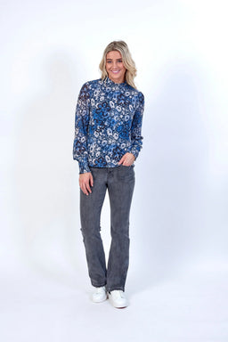 Woman wearing a blue floral long sleeve top, grey jeans, and white sneakers on white background
