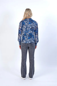 Woman in long sleeve blue floral blouse and grey jeans, standing with back to camera