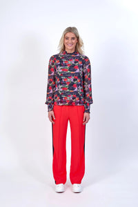 Woman wearing long sleeve floral print top with bright red wide-leg trousers and white sneakers