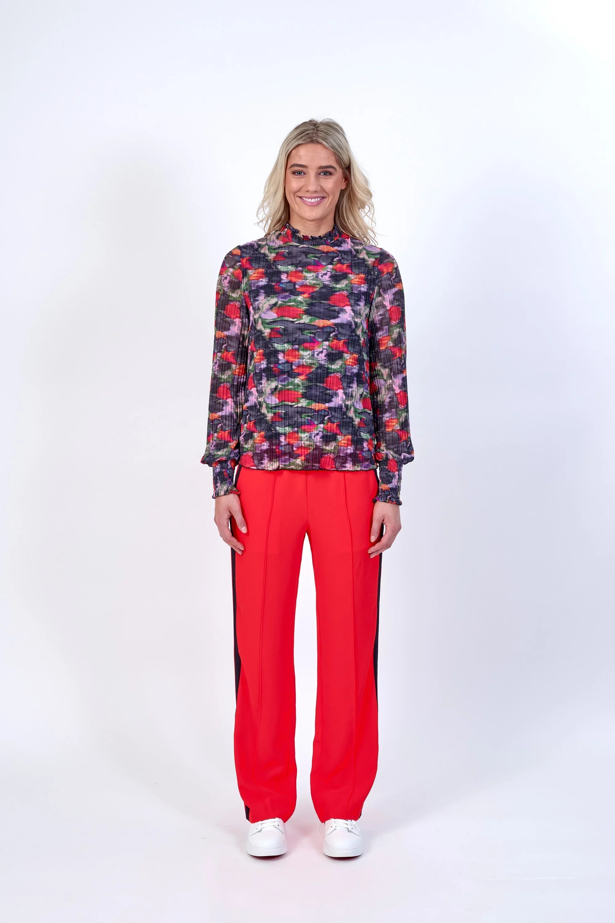 Woman wearing long sleeve floral print top with bright red wide-leg trousers and white sneakers