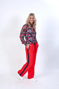 Woman in colorful floral long sleeve top and bright red pants with black stripe, white sneakers