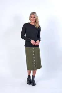 Woman wearing a black ribbed long sleeve top with gold cuff buttons and an olive green button-front midi skirt.