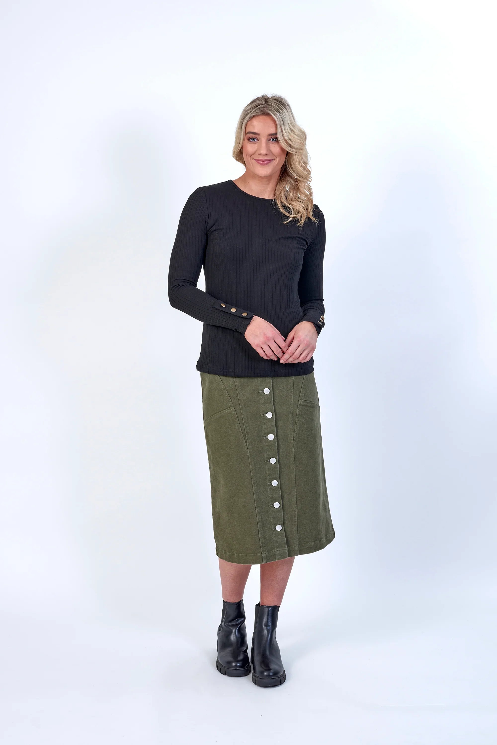 Woman wearing a black ribbed long sleeve top with gold cuff buttons and an olive green button-front midi skirt.