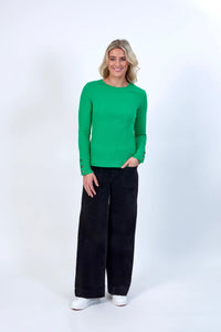 Woman in green ribbed long sleeve top with buttoned cuffs, black wide-leg pants, white sneakers