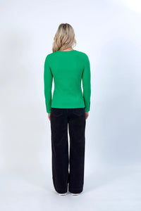 Woman in green ribbed long sleeve top and black wide-leg pants, back view, studio setting