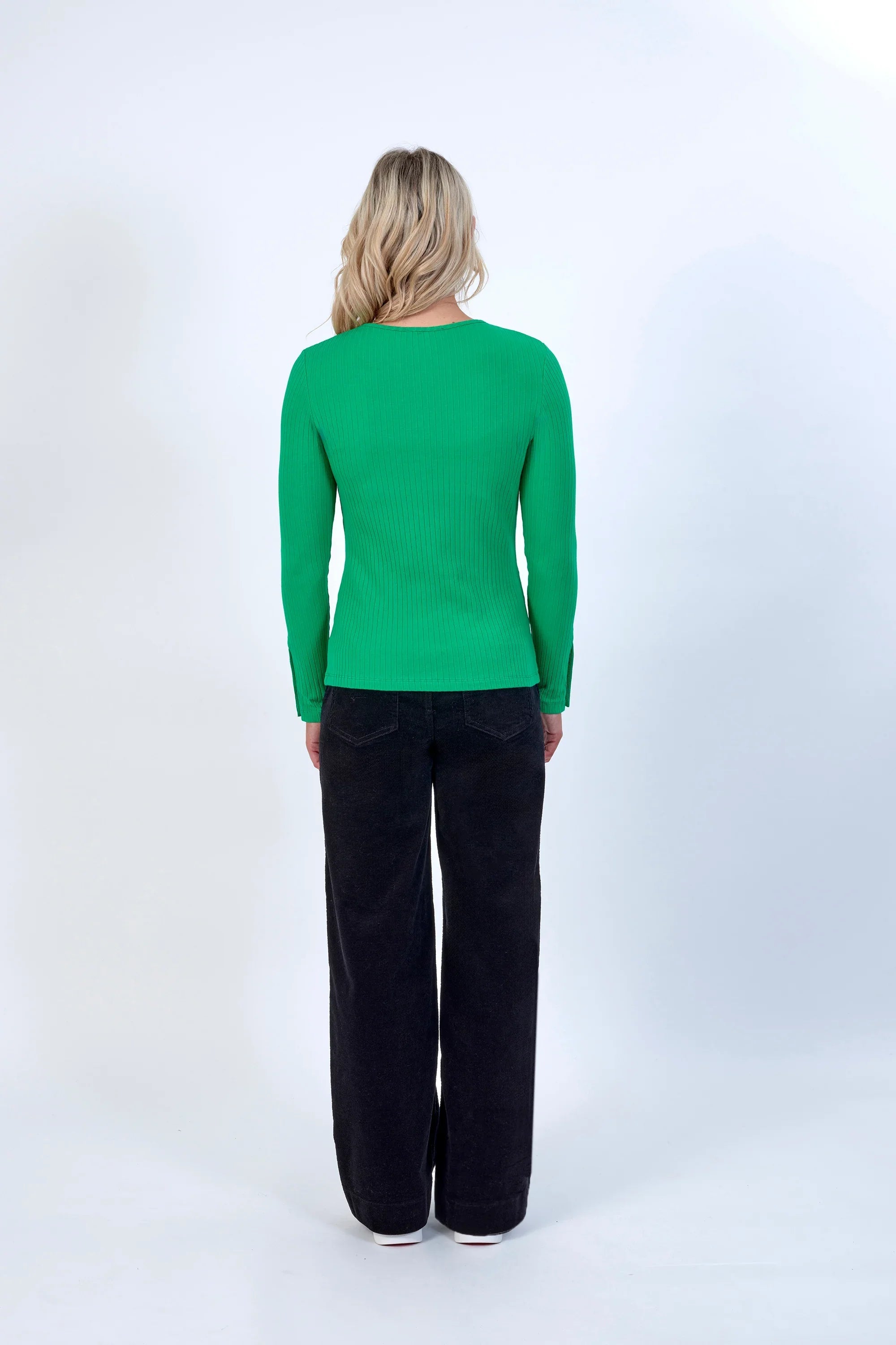 Woman in green ribbed long sleeve top and black wide-leg pants, back view, studio setting
