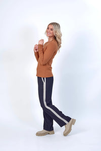 Woman wearing ribbed brown long sleeve top, navy pants with taupe stripe, and beige boots