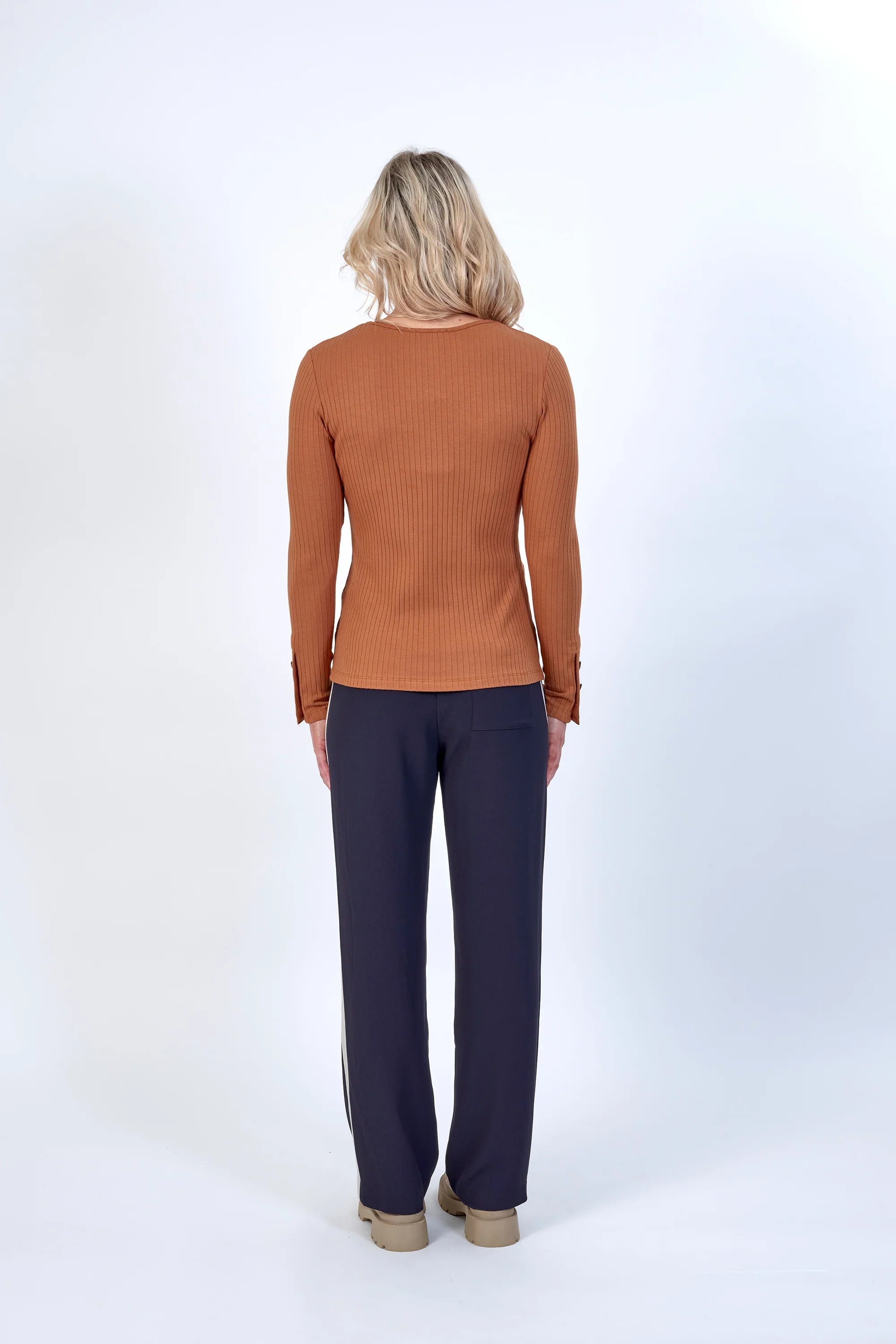 Woman wearing a ribbed brown long sleeve top and navy wide-leg pants, back view