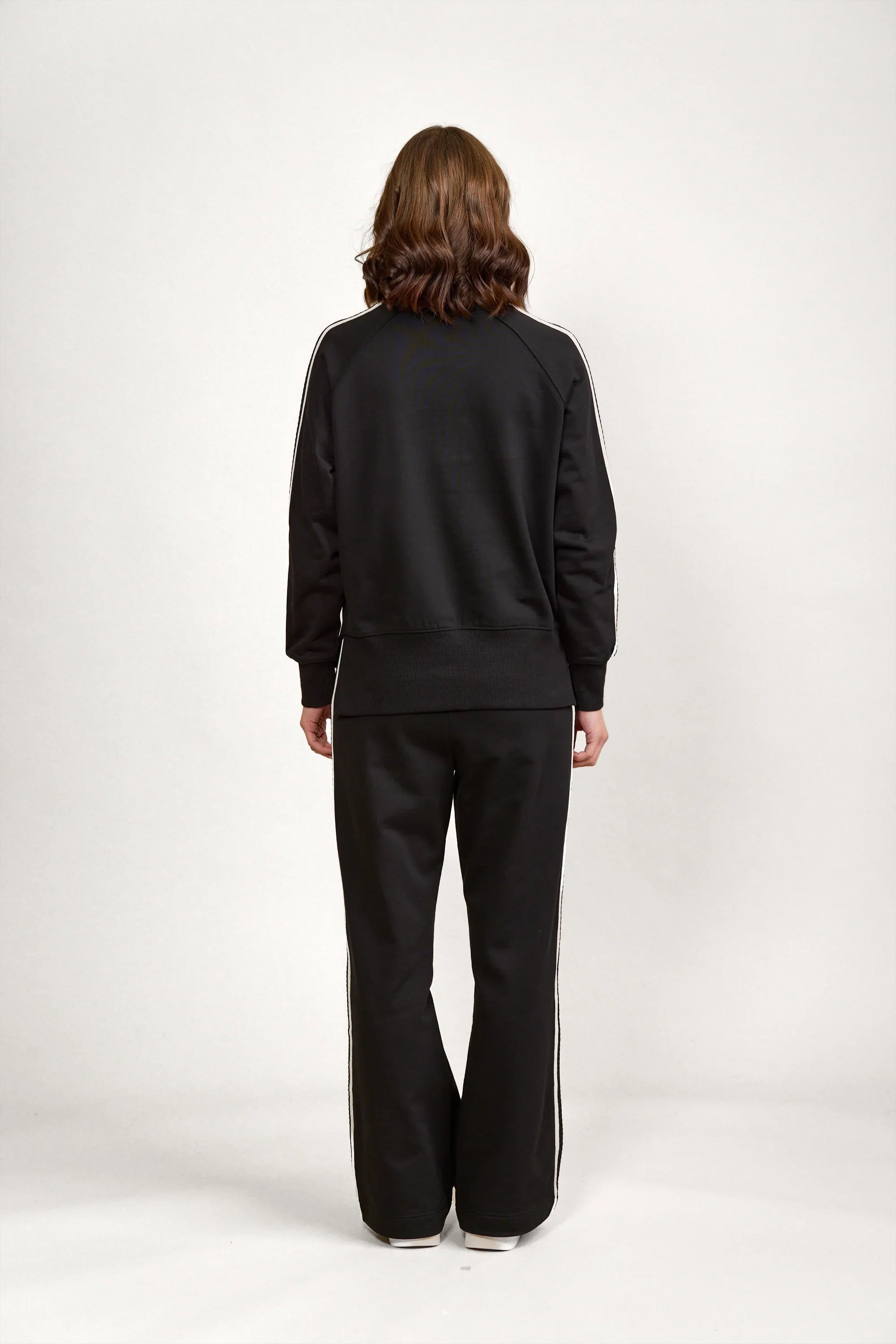 Back view of a woman wearing a black jumper and black pants with white side stripes
