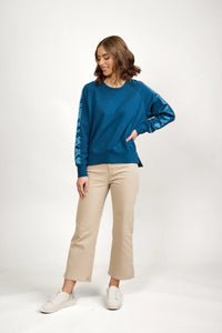 Woman in teal long sleeve jumper with satin sleeve panels, beige pants, and white sneakers