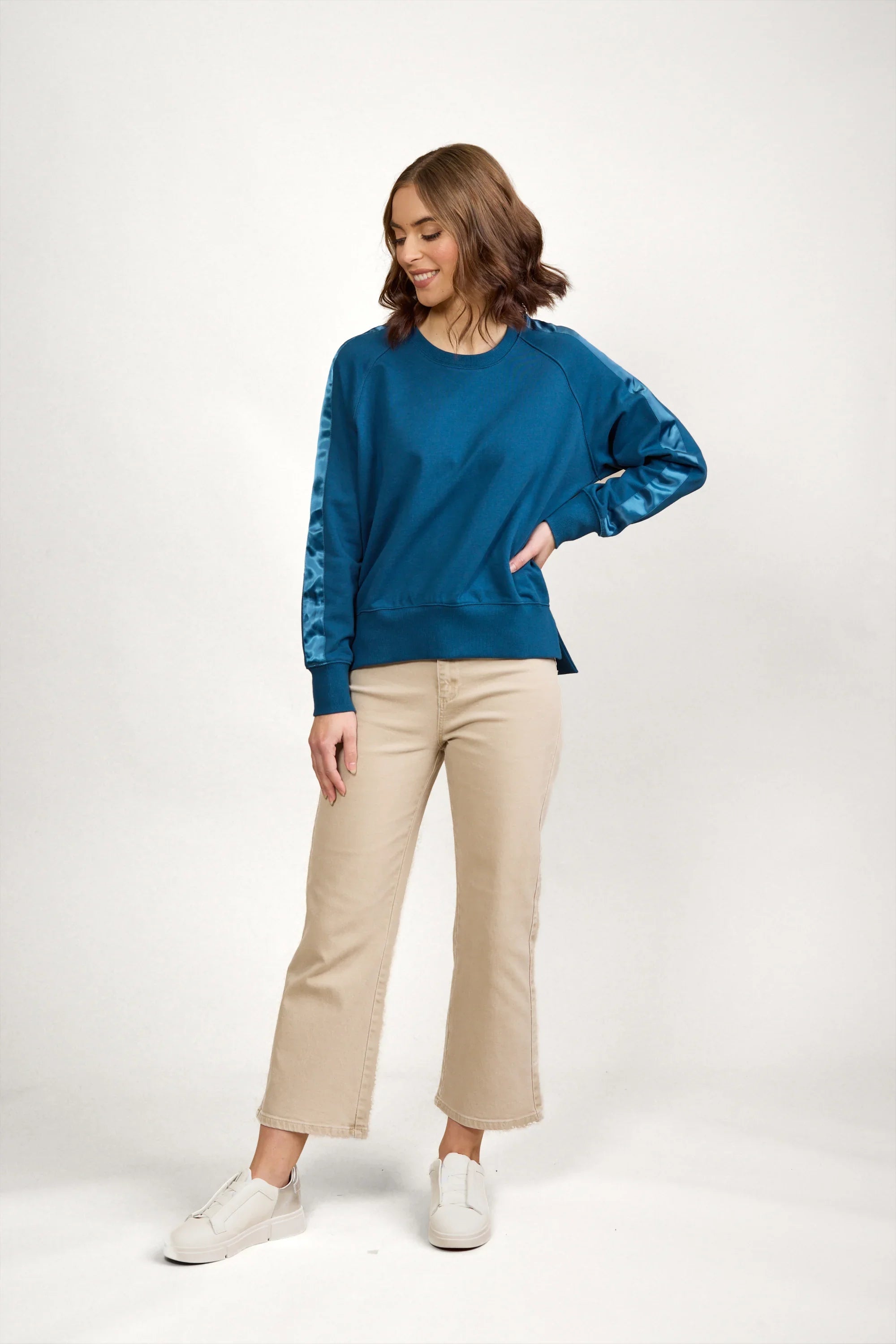 Woman in teal long sleeve jumper with satin sleeve panels, beige pants, and white sneakers