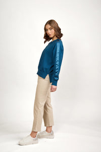 Woman wearing teal knit jumper with satin stripe sleeves, beige pants, and white sneakers