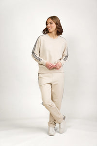 Woman wearing beige jumper and matching pants with black side stripe detail, white sneakers