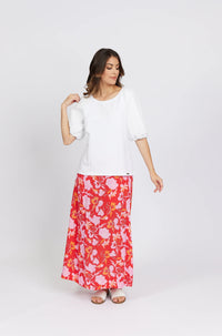 Woman wearing a white puff sleeve top and red floral maxi skirt, standing in studio