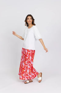 Woman wearing white puff sleeve top and red floral maxi skirt with white sandals