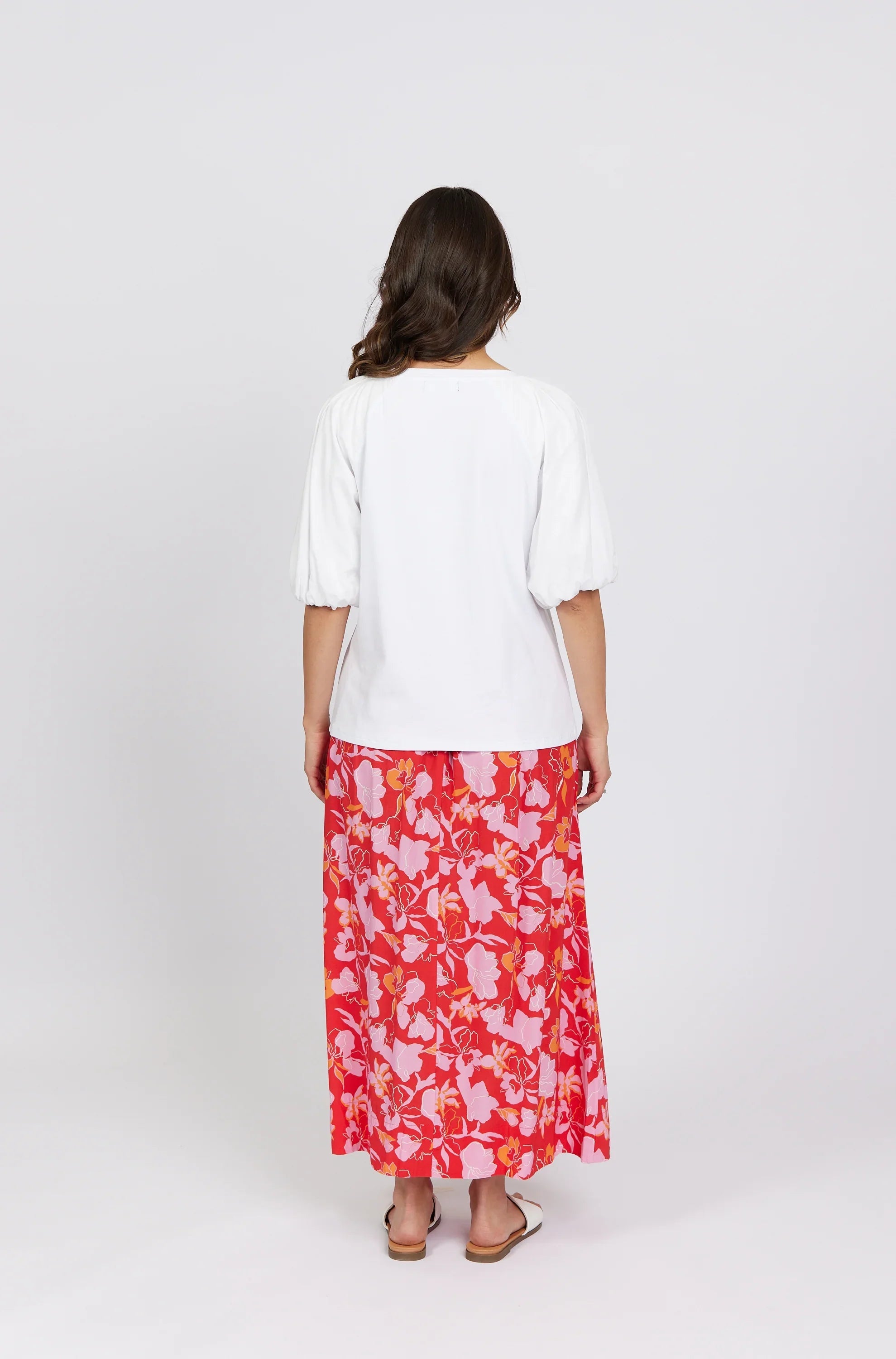 Woman wearing a white puff sleeve top and red floral midi skirt, back view