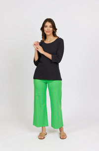 Woman wearing a black 3/4 sleeve top and bright green wide-leg pants, standing against white background.