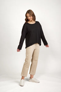 Woman in black long sleeve top with drop shoulders, beige wide-leg pants and white sneakers
