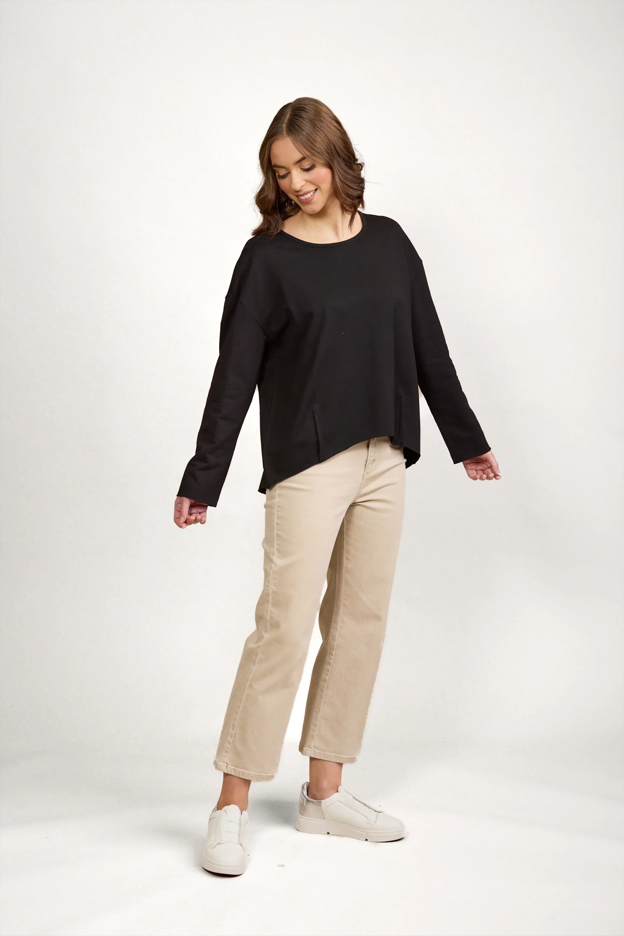 Woman in black long sleeve top with drop shoulders, beige wide-leg pants and white sneakers
