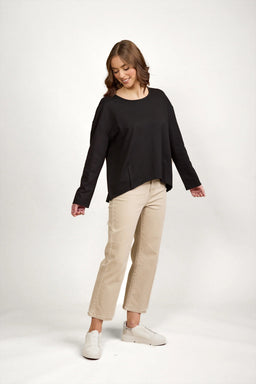 Woman in black long sleeve top with drop shoulders, beige wide-leg pants and white sneakers