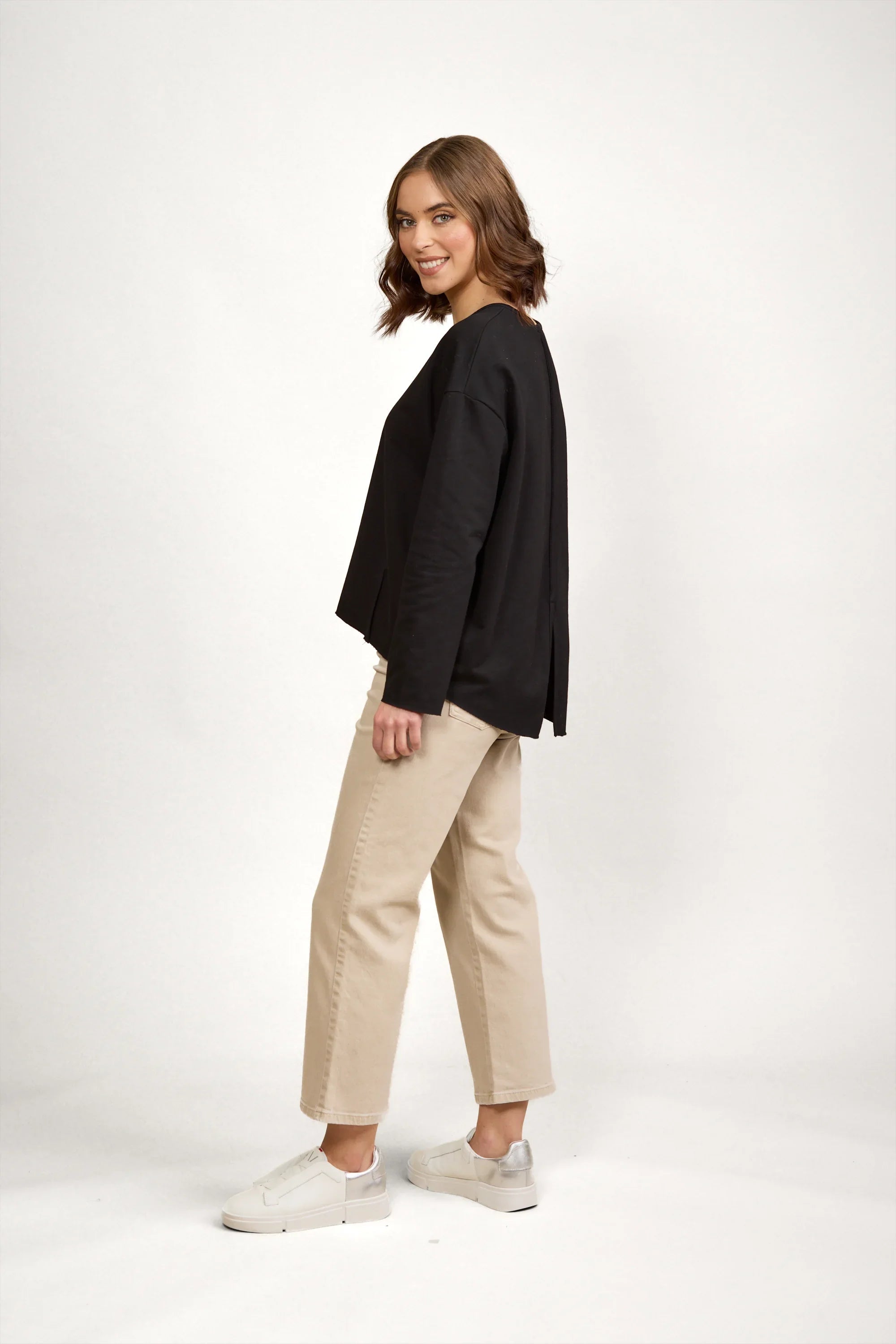 Woman wearing a relaxed black long sleeve top with beige wide-leg pants and white sneakers