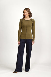 Woman wearing olive green long sleeve top with black stitching and wide leg dark jeans