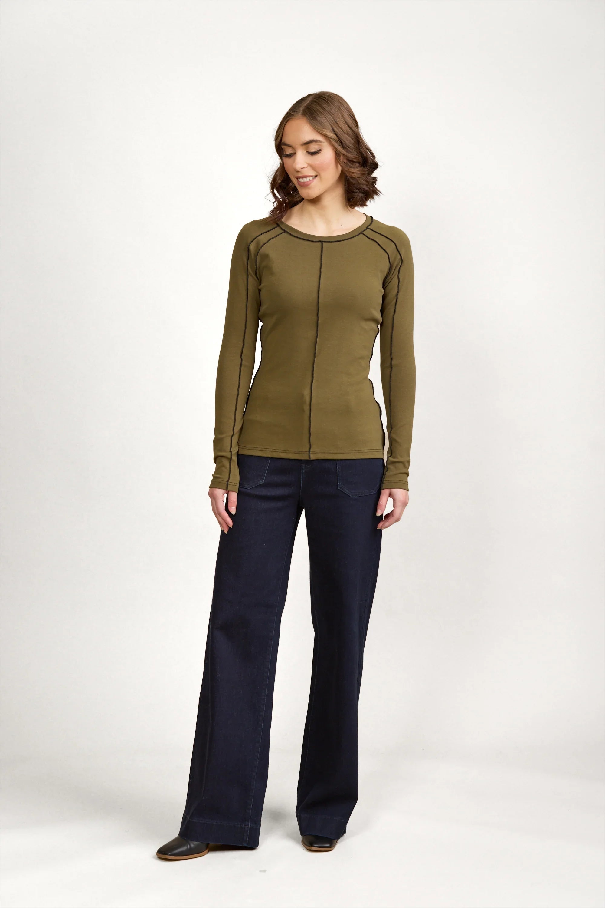 Woman wearing olive green long sleeve top with black stitching and wide leg dark jeans