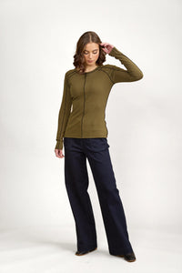 Woman wearing olive green long sleeve top with black contrast seams and wide-leg dark pants