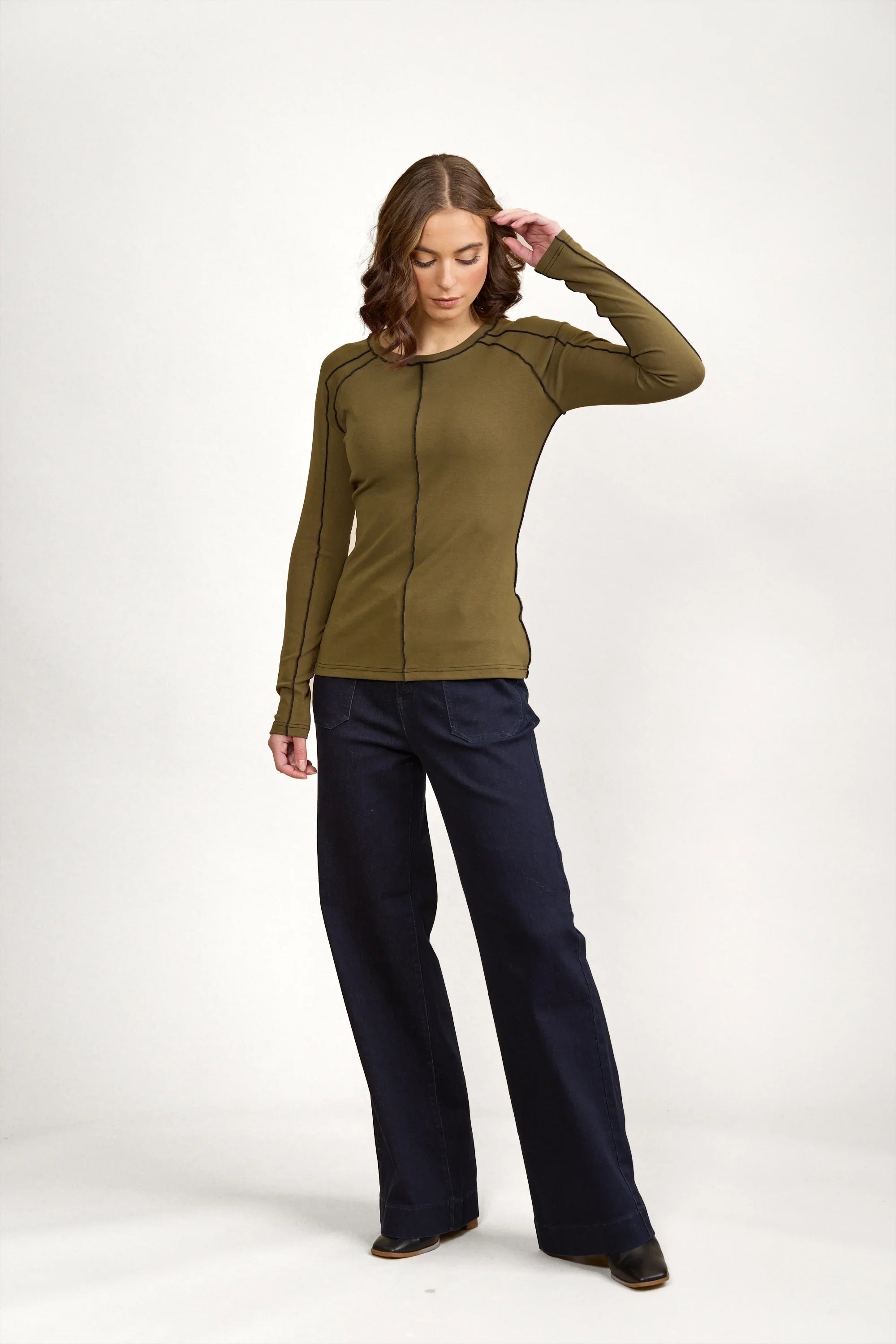 Woman wearing olive green long sleeve top with black contrast seams and wide-leg dark pants