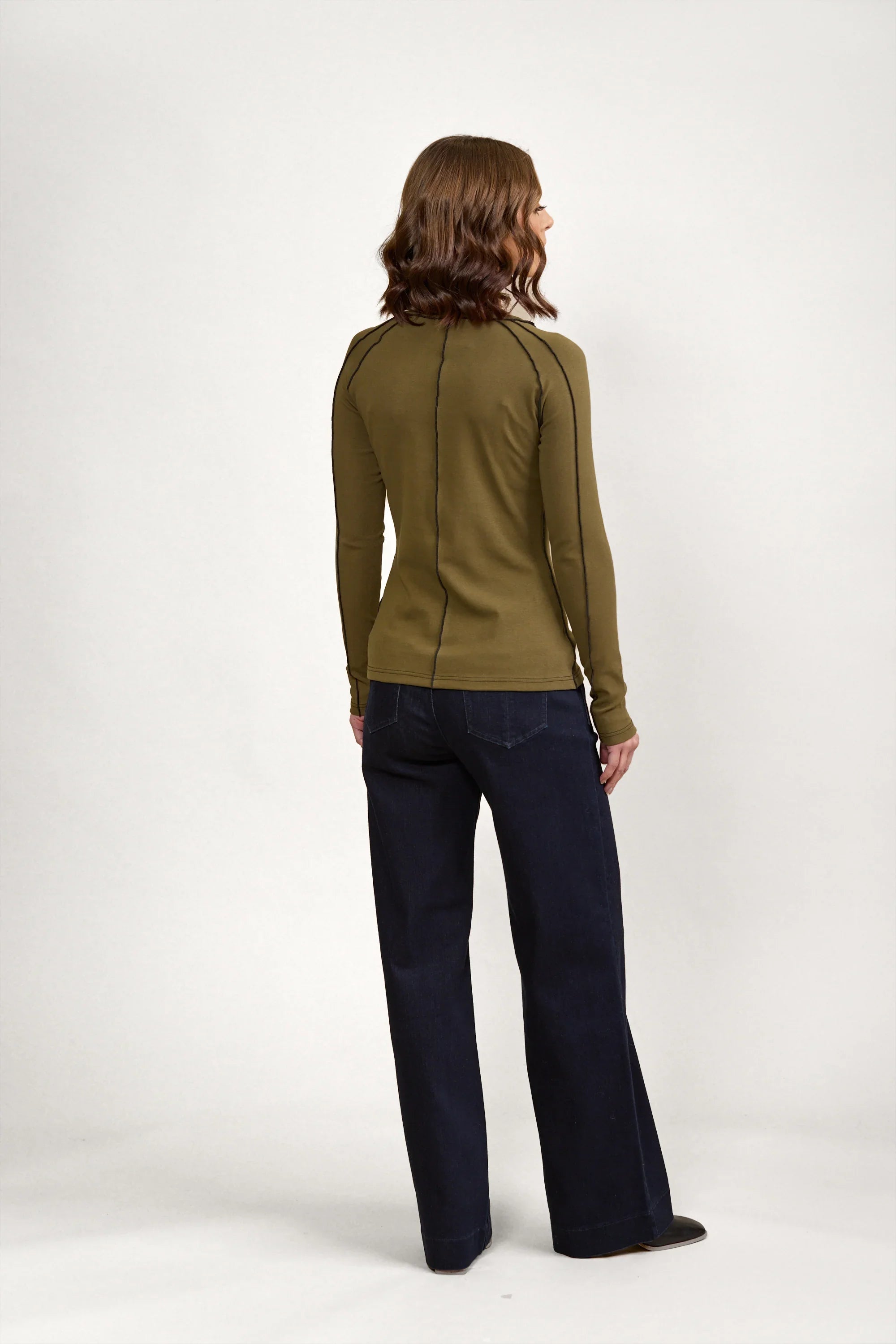 Woman wearing olive long sleeve top with black seam detail and dark wide-leg jeans, back view