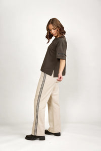 Woman wearing a dark green oversized tee and cream wide-leg pants with a patterned side stripe.