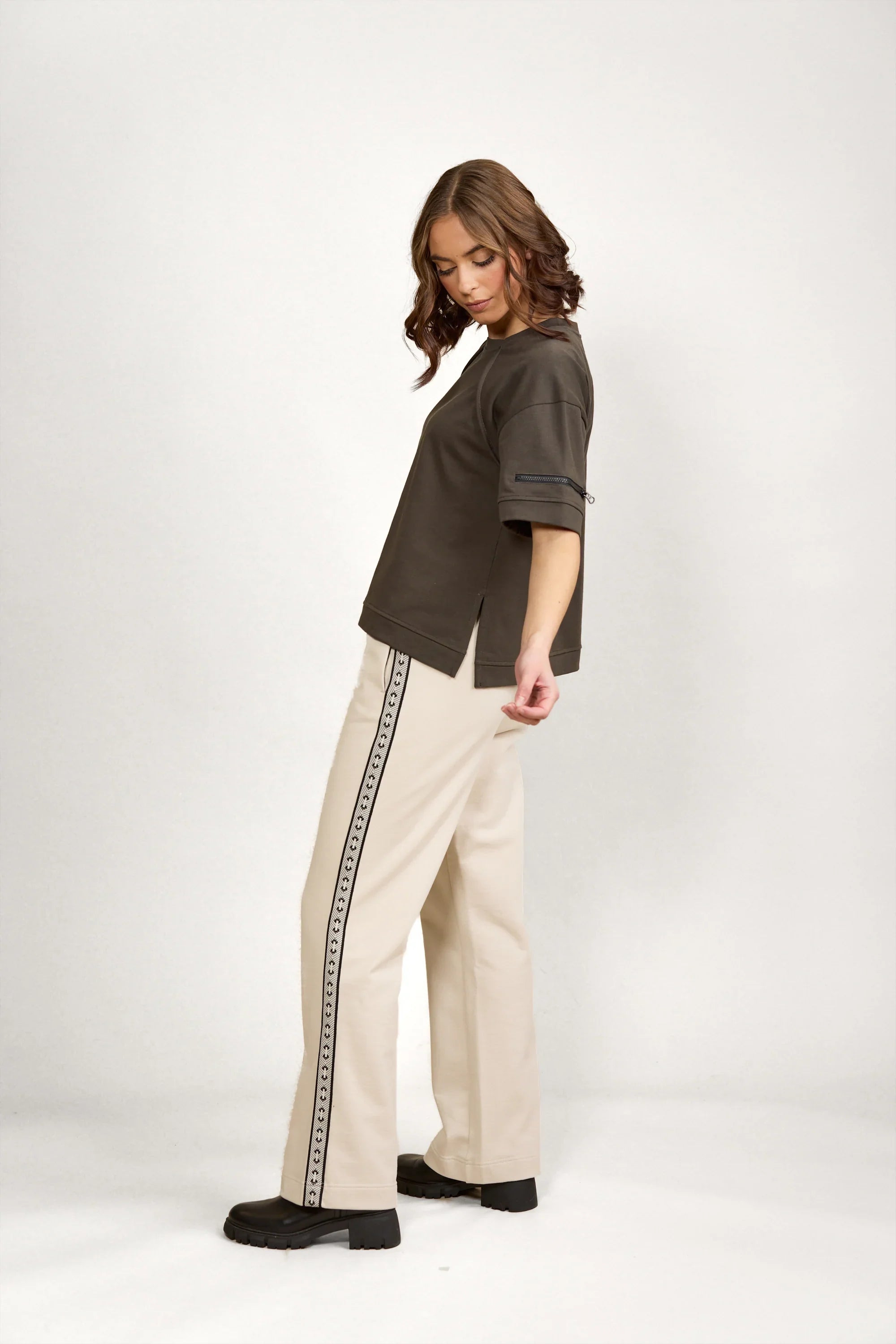 Woman wearing a dark green oversized tee and cream wide-leg pants with a patterned side stripe.
