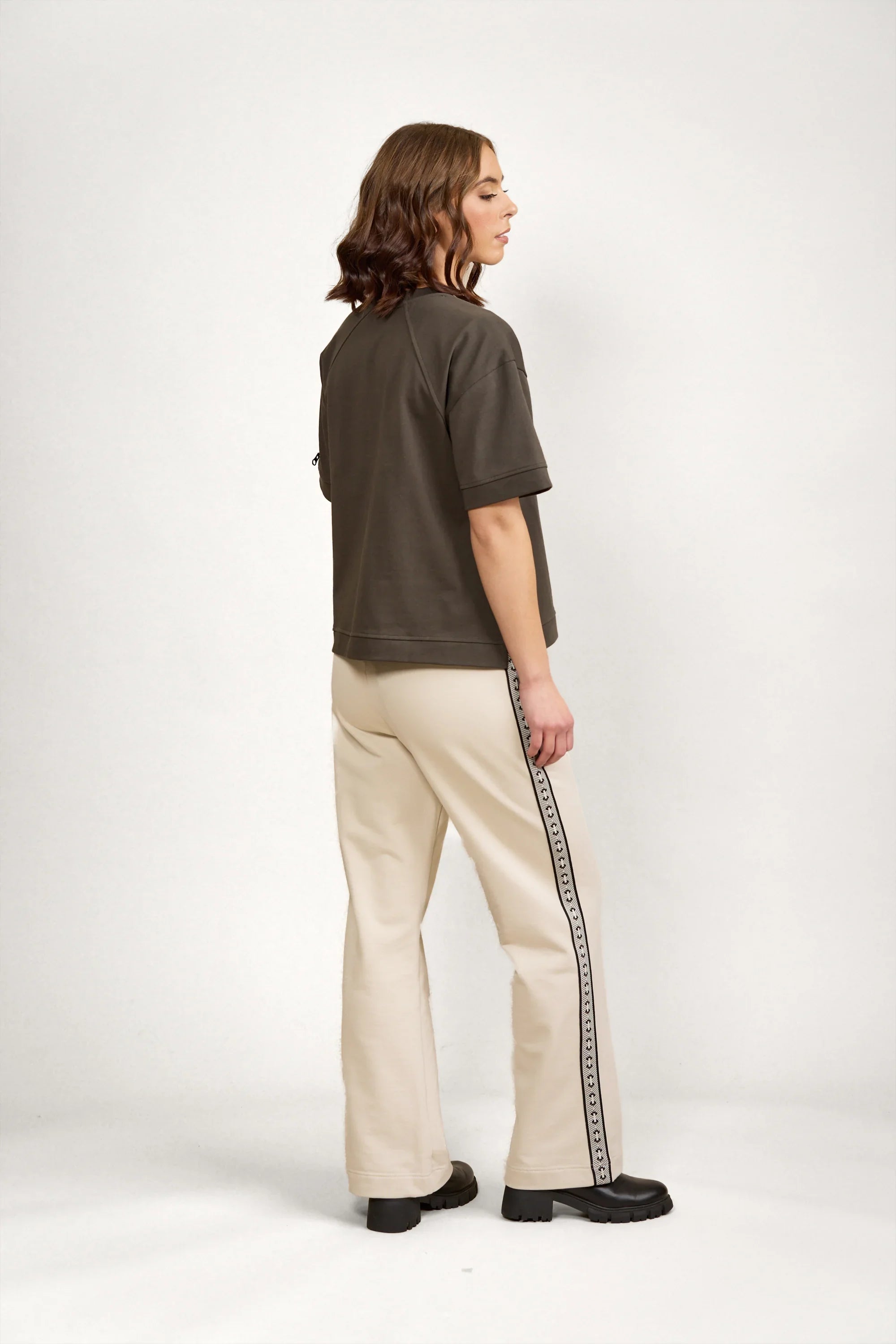 Woman wearing oversized khaki tee and cream track pants with logo side stripe in studio