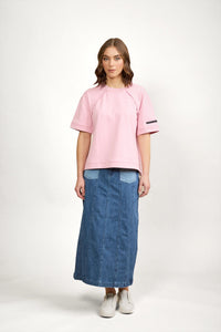 Woman wearing a pink short sleeve tee with patch detail and a denim maxi skirt, white sneakers