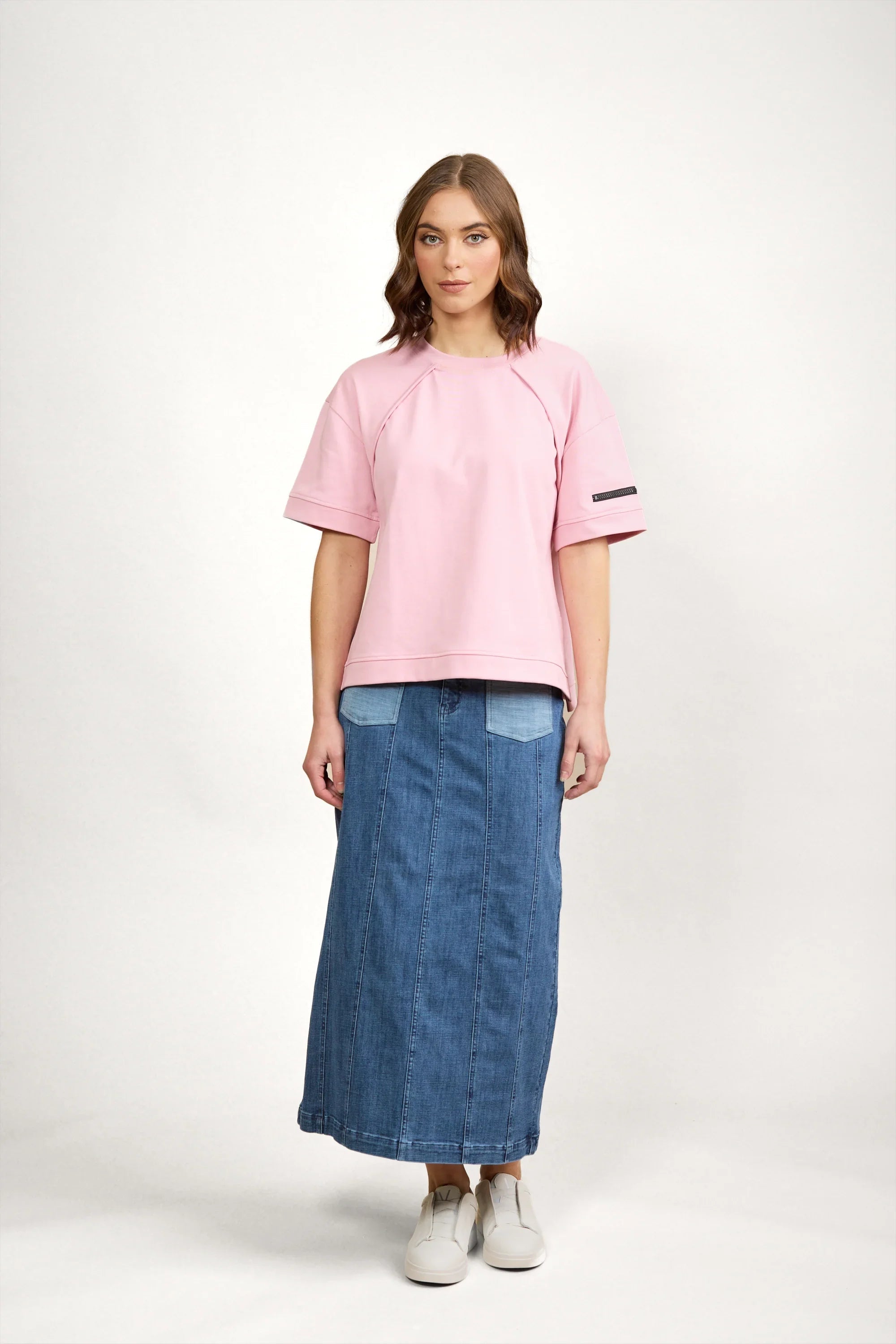 Woman wearing a pink short sleeve tee with patch detail and a denim maxi skirt, white sneakers