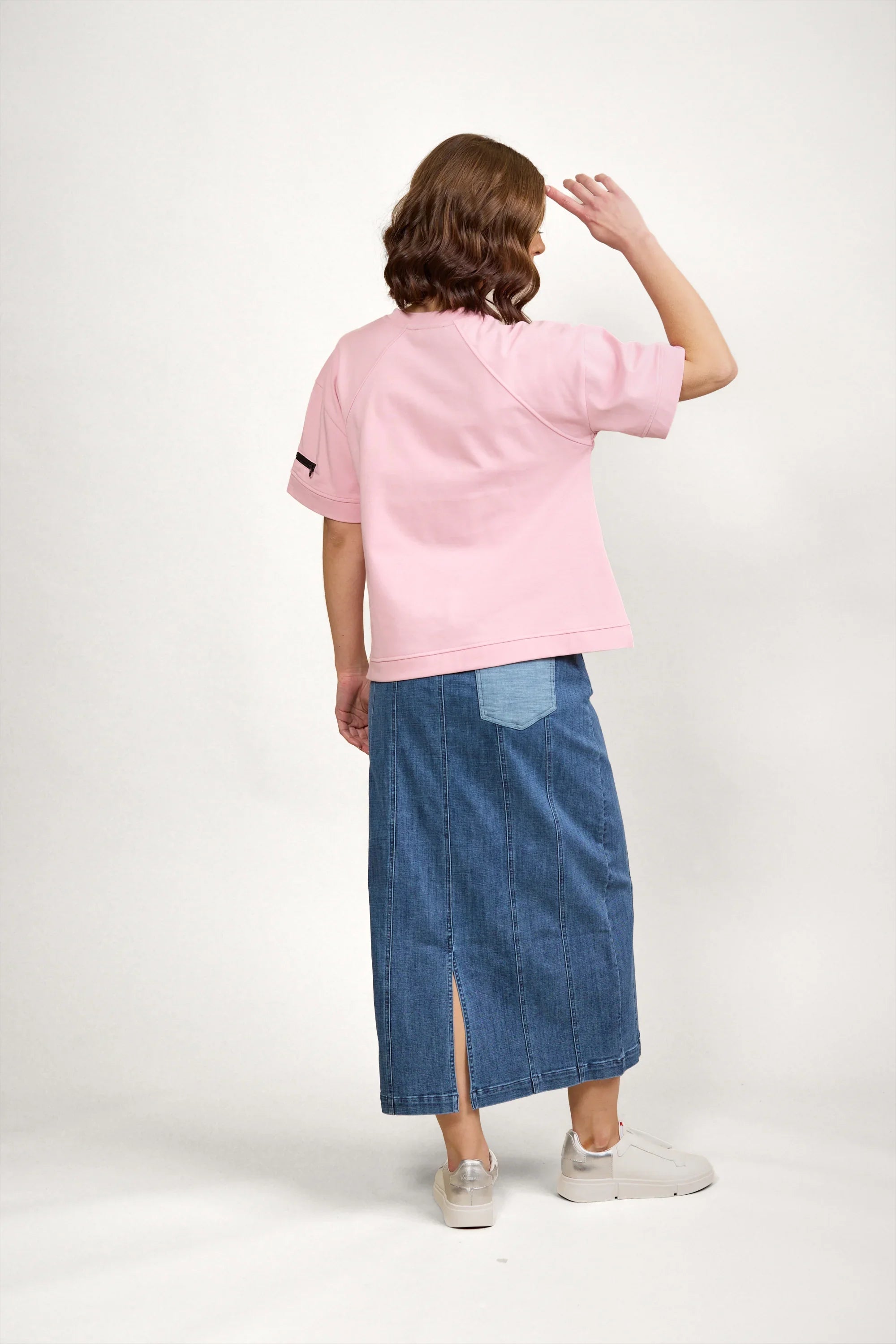 Woman wearing pink short sleeve tee and long denim skirt with back slit, standing indoors