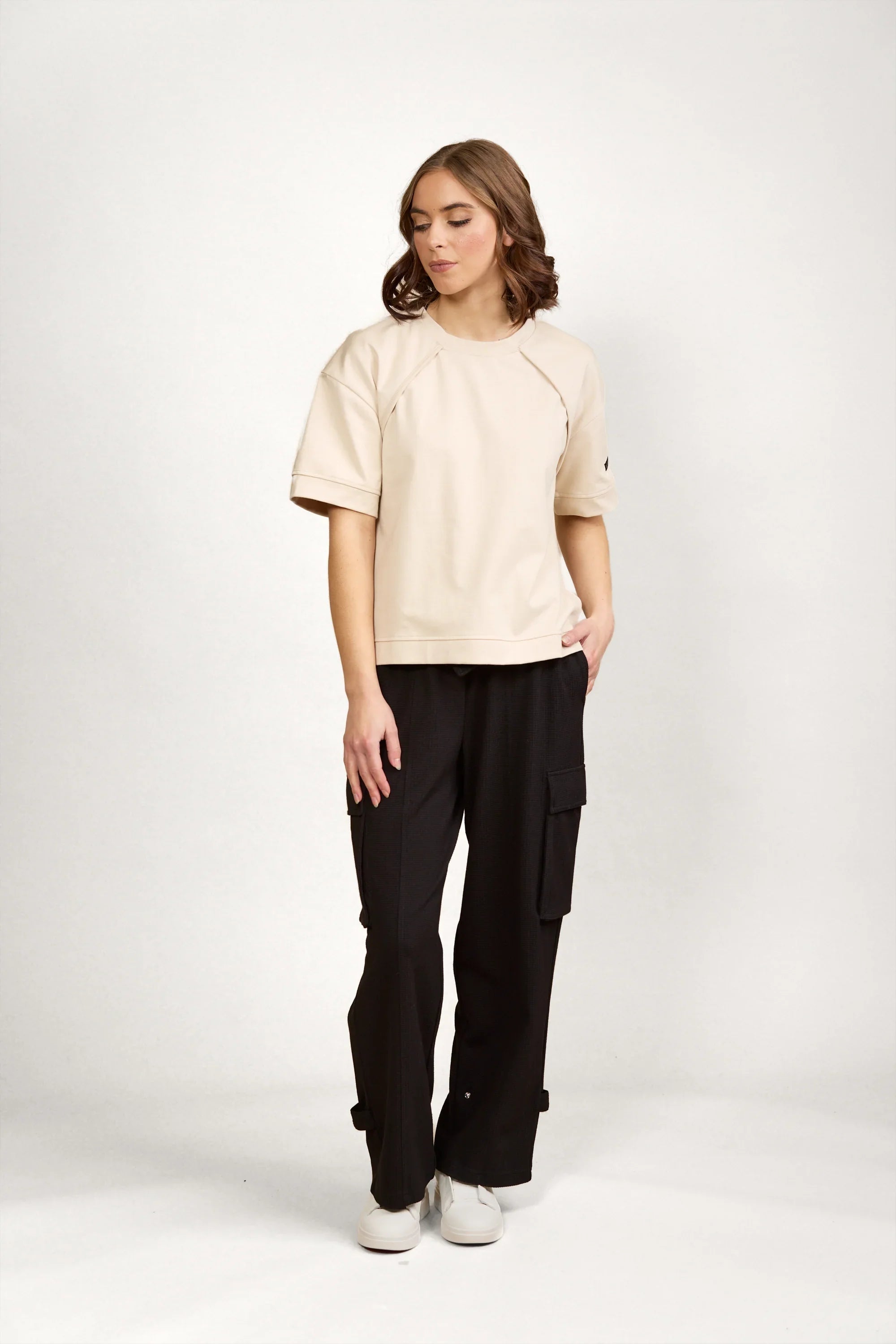 Woman wearing a stone beige short sleeve tee and black cargo pants, standing indoors