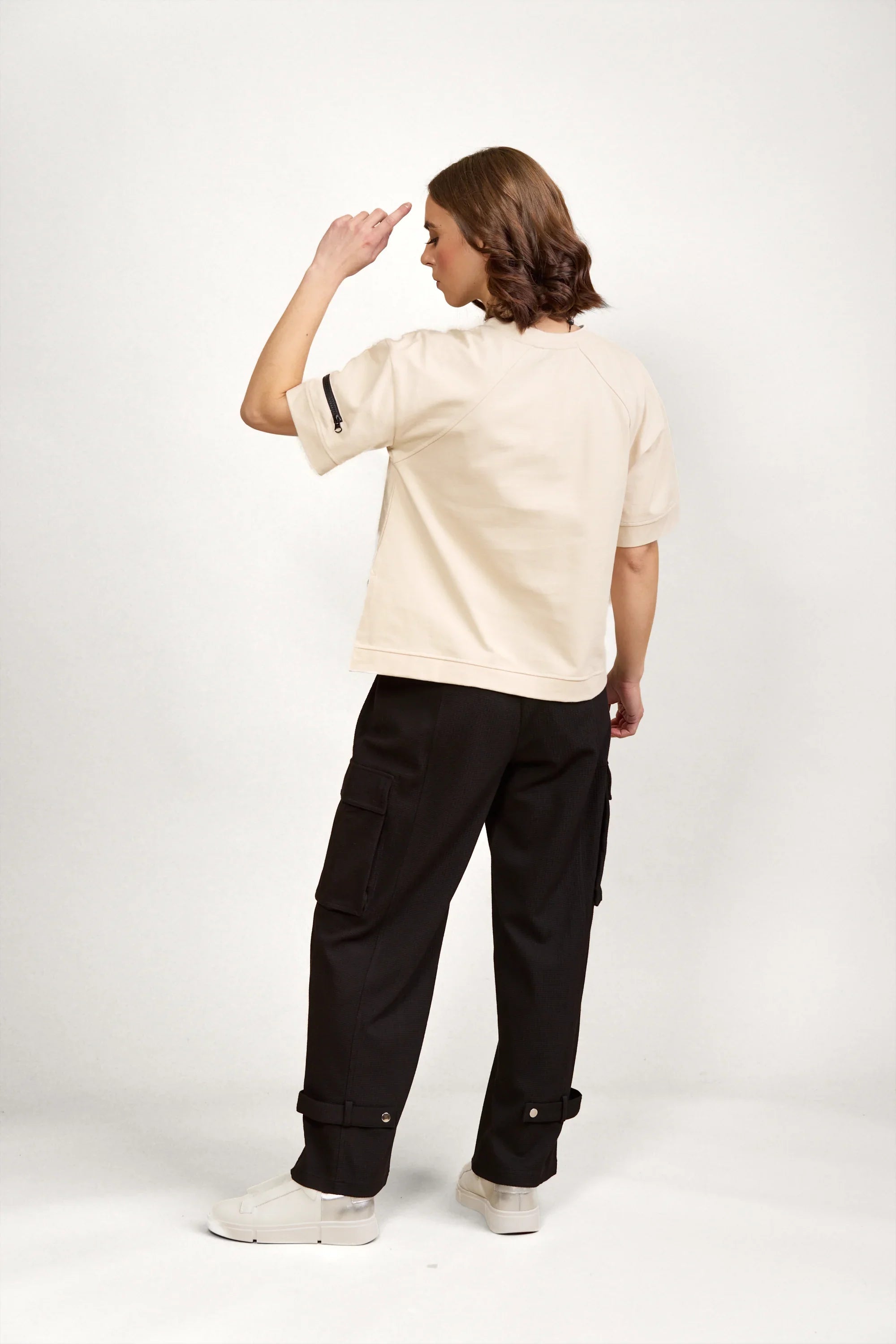 Model in beige short sleeve tee with arm zip pocket, black cargo pants, white sneakers