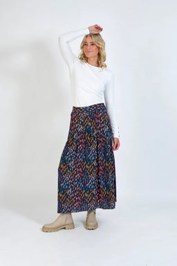 Woman in white long sleeve top, colorful patterned pleated maxi skirt, and beige boots