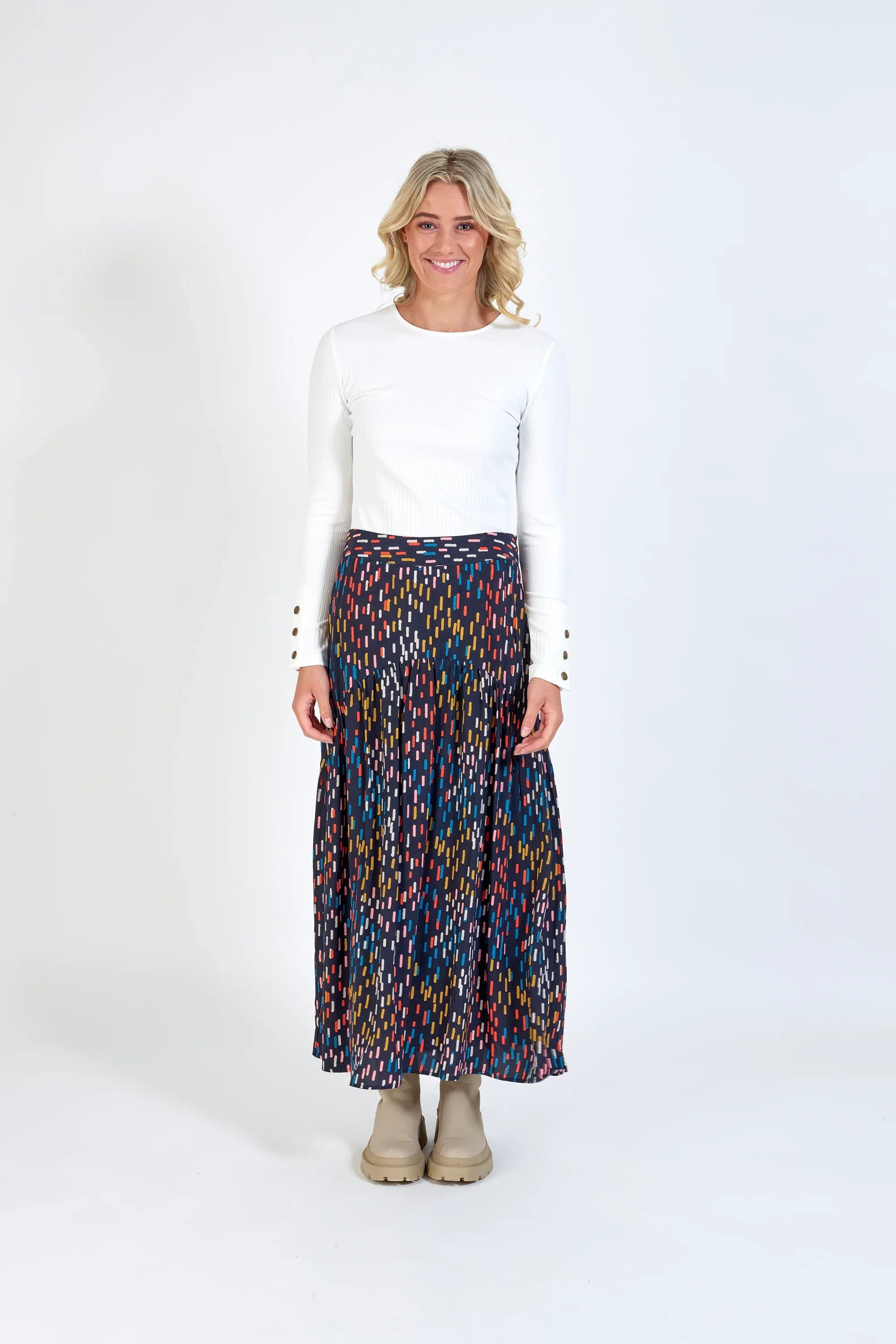 Woman in a white long-sleeve top and colorful patterned maxi skirt, standing indoors