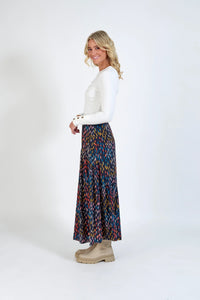 Woman in white long-sleeve top and colorful patterned maxi skirt with beige boots