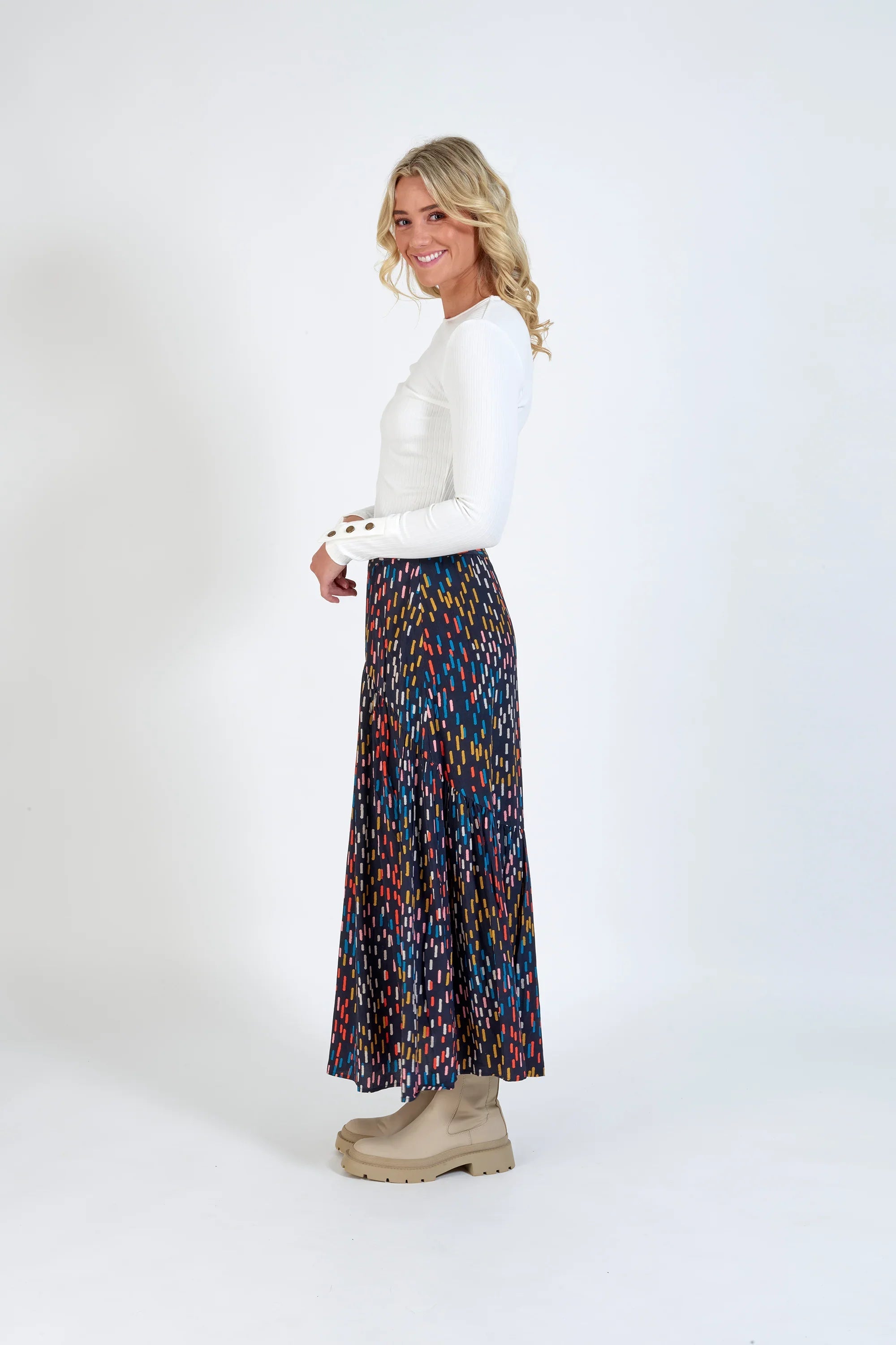 Woman in white long-sleeve top and colorful patterned maxi skirt with beige boots
