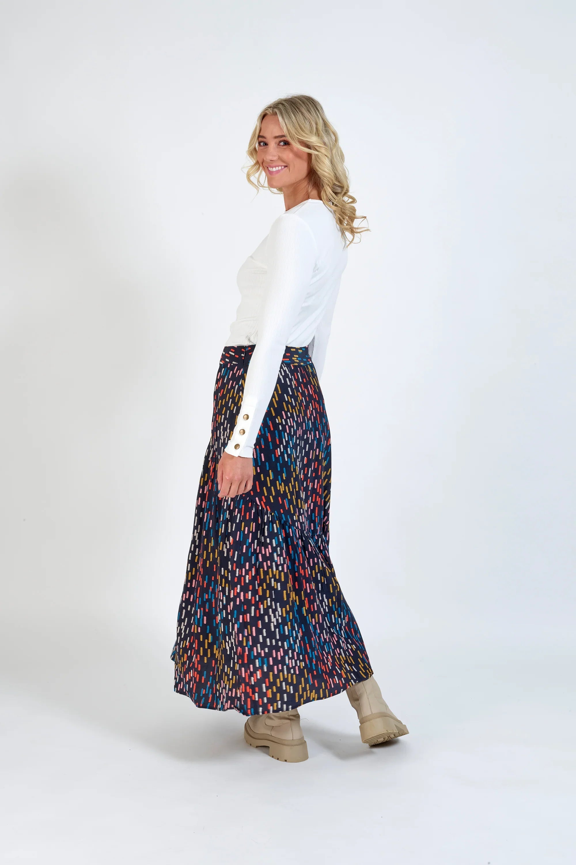 Woman wearing a white long-sleeve top and colorful printed maxi skirt with beige boots