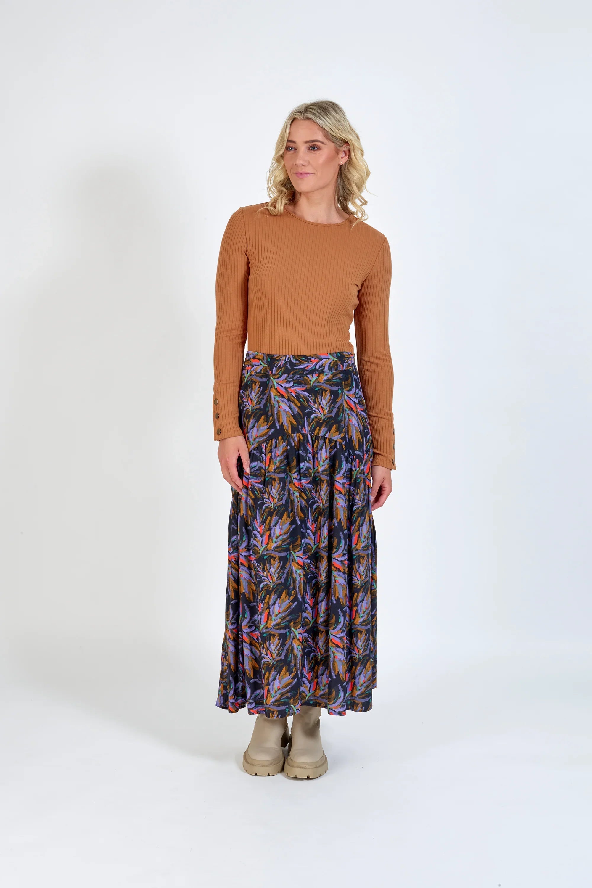 Woman wearing a tan ribbed top and a colorful floral maxi skirt with beige boots