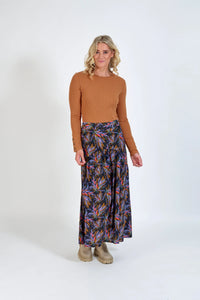Woman wearing a tan ribbed knit top and colorful floral maxi skirt, neutral background
