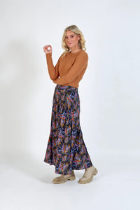 Woman in a brown long sleeve top and floral print maxi skirt with beige boots, studio background
