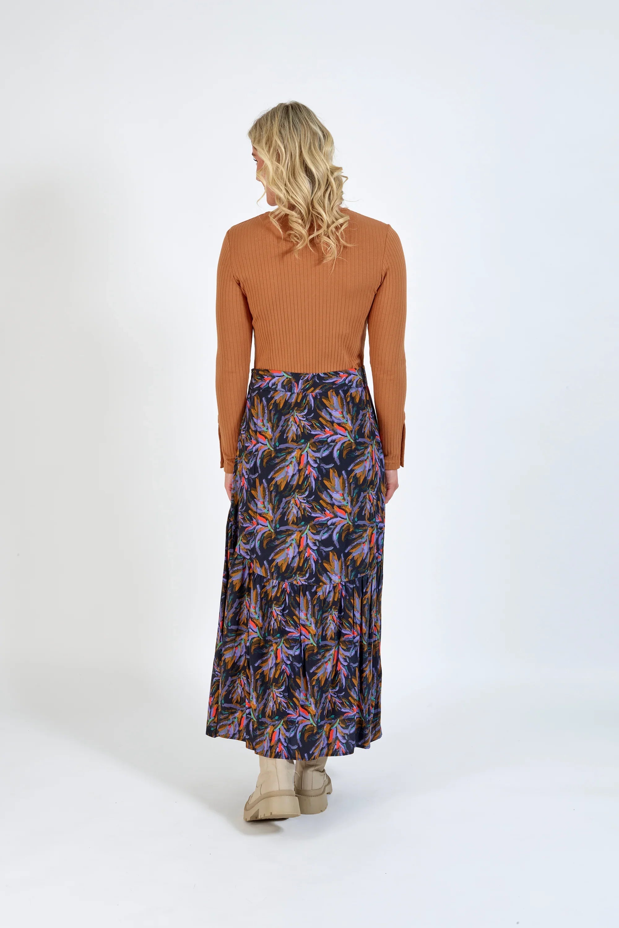 Woman wearing a ribbed brown long-sleeve top and a colorful floral maxi skirt, back view