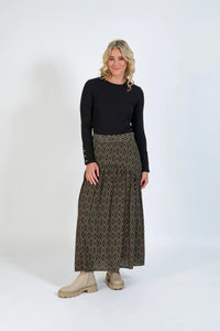 Woman wearing a geometric pattern maxi skirt, black long sleeve top, and beige boots