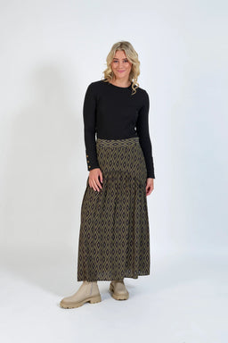 Woman wearing a geometric pattern maxi skirt, black long sleeve top, and beige boots