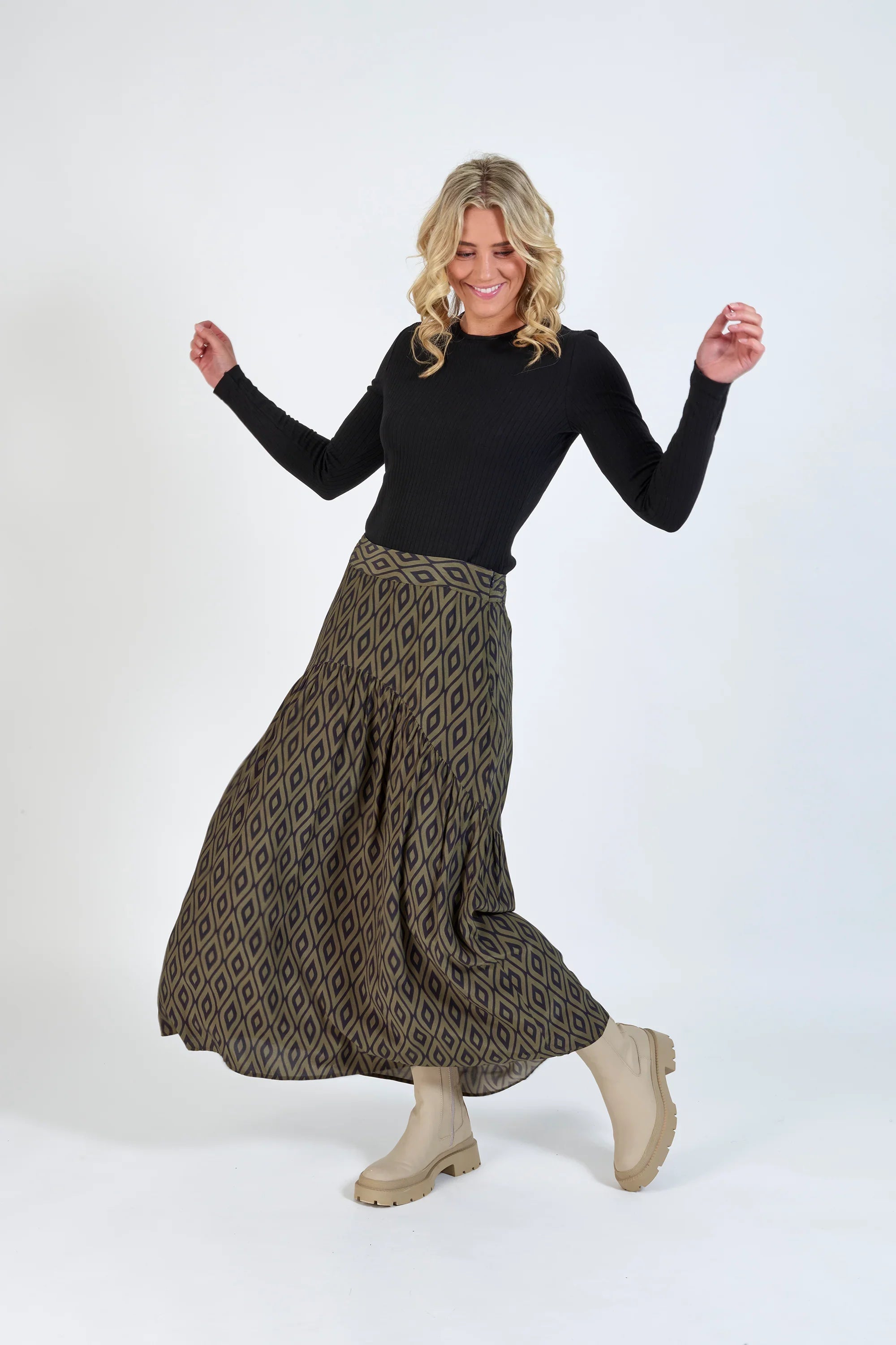Woman wearing a black long sleeve top, geometric print maxi skirt, and beige boots